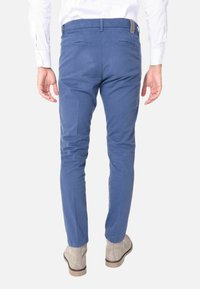 Chino blu, slim-fit, con tasche posteriori; realizzati in tessuto liscio; indossati con stivali alla caviglia beige e una camicia bianca.