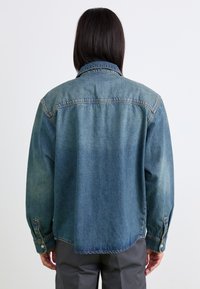 Denimjakke i lyseblå, med klassisk krave, knaplukninger ved ærmerne og en let oversized pasform med lige kant.