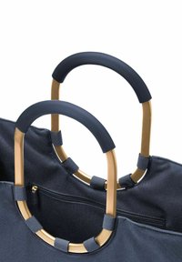 Sac en tissu bleu marine avec poignées courbes en or. Les poignées sont dotées de grips en caoutchouc noir. Poche zippée visible à l'intérieur du sac.