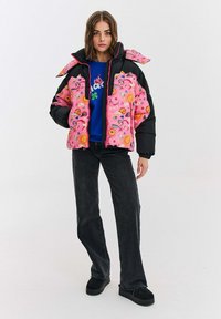 Svetloružová prešívaná bunda s čiernymi akcentmi, obsahujúca kvetinový a hviezdny vzor, so zipsovým uzáverom a vysokým golierom. Nosená s tmavými džínsami a topánkami.