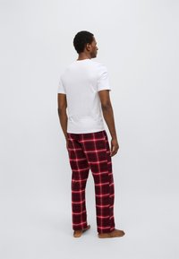 Ανδρικό λευκό κοντομάνικο μπλουζάκι σε συνδυασμό με κόκκινο καρό παντελόνι από φλάναλ. Το παντελόνι έχει βουρτσισμένη υφή και ίσια γραμμή στο πόδι.