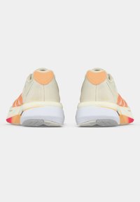 Pár béžovo-oranžových sportovních bot zobrazených zezadu s bílými podrážkami a texturovanými detaily na patě na bílém pozadí.