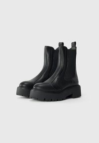 Bottines en cuir noir avec des panneaux élastiques sur les côtés, semelles en caoutchouc épaisses et un bout arrondi, ornées de détails de couture et de languettes.
