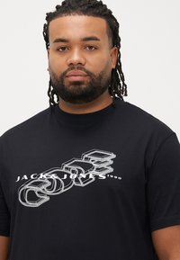 Sort kortærmet t-shirt med hvidt grafisk tryk "JACK & JONES 1990" i et lagdelt design. Fremstillet af blødt bomuldsstoffet.