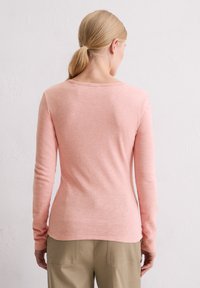 Langärmliges, tailliertes Oberteil aus weichem Pastellrosa-Stoff, mit einem runden Ausschnitt und einer glatten Textur. Keine sichtbaren Muster oder Verzierungen.