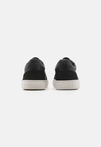 Black leather and suede sneakers with a cream rubber sole; features a smooth texture and subtle branding on the heel.
