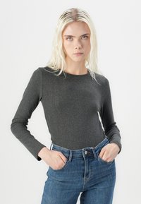Langermet, ribbet topp i mørk grå, kombinert med høy midje blå jeans. Tettsittende design med rund hals og strukturert stoff.