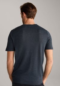 Granatowa koszulka z krótkim rękawem z okrągłym dekoltem. Miękka, teksturowana tkanina z delikatnym wzorem. Z tyłu widoczny dopasowany krój i gładkie szwy.