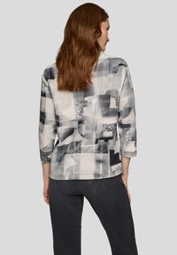 Dreiviertelarm-Oberteil mit abstraktem schwarz-grauem Muster auf hellem Stoff, mit abgerundetem Saum und lockerem Sitz.