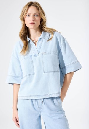 Lichtblauw denim overhemd met korte mouwen, een kraag, twee borstzakken en een losse pasvorm. Zachte textuur met zichtbare stiksel-details.