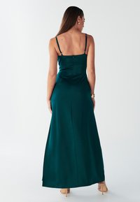 Abito lungo in satin color teal con spalline sottili regolabili e corpetto aderente. Presenta una zip nascosta sul retro e una silhouette fluida e morbida.
