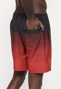 Costumi da bagno da uomo in gradiente nero e rosso, caratterizzati da strisce orizzontali, cintura elastica e tasche laterali per riporre gli oggetti.