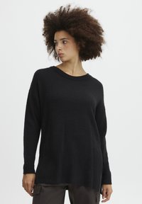 Schwarzer Pullover mit geripptem Saum und Bündchen, langen Ärmeln und entspannter Passform. Die Textur wirkt weich und gestrickt.