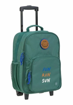 Sac à dos à roulettes vert foncé avec un patch smiley, une poche avant zippée, une poche latérale en filet et un texte imprimé : "FUN RUN SUN."