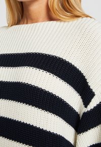 Maglione lavorato a maglia con strisce orizzontali blu navy e crema. Il tessuto presenta un motivo testurizzato a coste con un ampio scollo.
