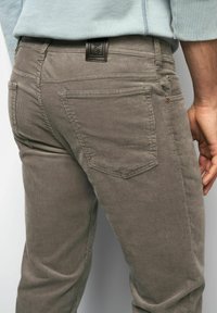 Grey corduroy pants with a slim fit, featuring back pockets and a leather tag at the waistband. Subtle ribbed texture throughout.
