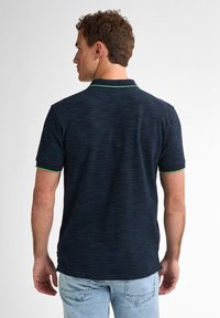 Camisa polo de color marino con acentos verdes, con un patrón texturizado y un corte ajustado. Se aprecian las mangas cortas y un cuello clásico.