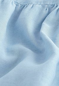 Tissu bleu clair avec des coutures froncées créant des plis doux et une texture, montrant un gros plan de matériau textile tissé.