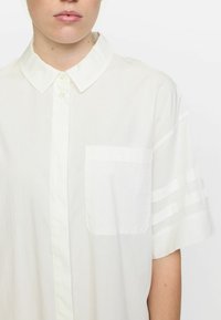 Witte korte mouwen blouse met een geknoopte kraag, een enkele borstzak en horizontale gestreepte accenten op de mouwen. Zachte textuur, lichtgewicht stof.