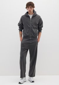 Felpa grigia con zip e tasche frontali, abbinata a pantaloni coordinati. Realizzata in tessuto morbido, presenta una vestibilità comoda e polsini a costine.