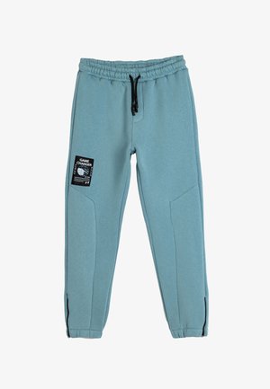 Hellblaue Jogginghose aus weichem Material, mit Kordelzugbund, Seitentaschen und einem schwarzen „GAME CHANGER“-Label am Bein.