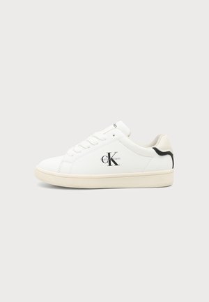 Baskets basses blanches Calvin Klein avec logo noir sur le côté et accent noir au talon, semelle beige et lacets blancs sur fond uni.