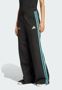 Crne trenirke s opuštenim krojem, s tirkiznim bočnim prugama i bijelim Adidas logom. Izrađene su od mekog, udobnog materijala.