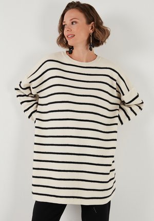Maglione oversize a righe crema e nere con scollo ampio, maniche larghe e tessuto morbido e testurizzato. Abbinato a pantaloni neri.