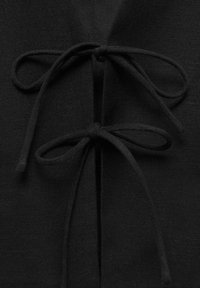 Deux liens en tissu noir noués en nœuds sur une fente verticale sur un tissu noir texturé.