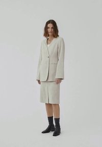 Lichtbeige op maat gemaakte blazer met een v-hals en enkele knoopsluiting, gecombineerd met een knie-lange kokerrok. Draag met zwarte enkellaarzen.