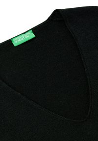 Czarny sweter w serek z zielon ą etykietą "United Colors of Benetton" wszytą w pobliżu dekoltu na białym tle.