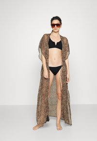 Kimono com padrão de leopardo, feito de tecido leve, com frente aberta e mangas curtas, sobre um biquíni preto. Tons de castanho e bege.