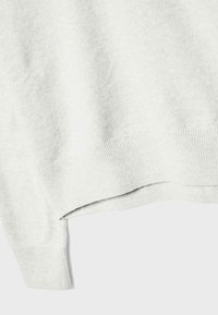 Gros plan sur un tissu de pull en maille gris clair montrant les détails des poignets et de l'ourlet côtelés.