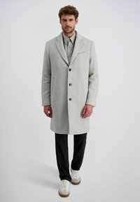 Lichtgrijze wollen blend jas met notch-lapel, drie knopen, zijzakken en een gestructureerde stof, gecombineerd met zwarte broeken en witte sneakers.