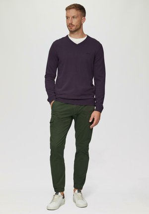 Lila V-Ausschnitt-Pullover, grüne Cargo-Hose mit elastischen Bündchen und weiße Sneakers. Einfaches Design mit lässigem Schnitt und minimalen Details.