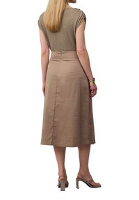 Top in maglia beige e marrone chiaro, con maniche corte; abbinato a una gonna A-line di lunghezza ginocchio in tessuto liscio marrone chiaro e sandali con tacco a blocco.