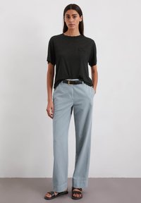 Zwart T-shirt met korte mouwen en een zak, gecombineerd met lichtblauwe wijd-uitlopende broeken en zwarte sandalen met een gesp. Glad stofgevoel.
