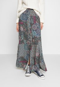 Jupe longue à motifs avec des designs complexes en bleu, rouge et blanc, dotée d'une fente sur le devant. Assortie avec des baskets navy.
