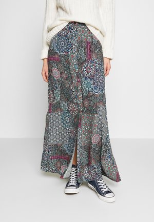 Jupe longue à motifs avec des designs complexes en bleu, rouge et blanc, dotée d'une fente sur le devant. Assortie avec des baskets navy.
