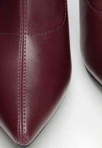 Bordó kožené boty se špičatou špičkou, s viditelným šitím a hladkou texturou na bílém pozadí.