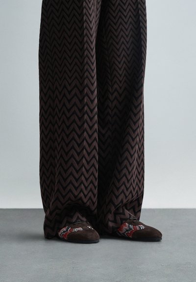 Pantalons larges à motif zigzag brun associés à des chaussures slip-on brunes et à motifs avec des accents rouges, bleus et crème.