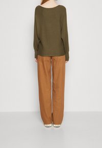 Olive green, loose-fitting ribbed sweater with wide neckline, paired with brown wide-leg trousers. Soft fabric, minimal design details.