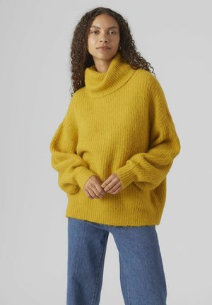 Yellow knitted sweater with a high collar, ribbed texture, and loose sleeves, paired with light blue, wide-leg jeans.