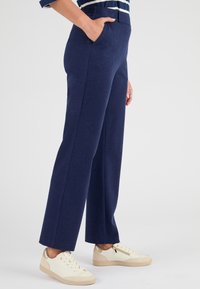 Pantaloni blu navy, su misura, con taglio dritto, texture morbida e tasche laterali, abbinati a sneaker crema e beige.