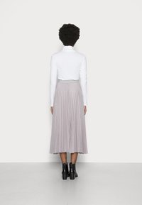 Witte lange mouwen top gecombineerd met een geplooide, lichtgrijze rok tot de knie en zwarte enkellaarsjes, die gladde texturen en een vloeiende ontwerp tonen.