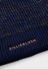 Marineblå strikket hue med metalltråd accenter. Har tekstureret ribstrik og et pink logo label "BILLIEBLUSH" på kanten.