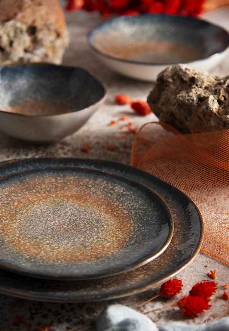 Steingut-Geschirrset mit einem Farbübergang von dunkelblau zu braun, strukturierten Oberflächen und kontrastierenden metallischen Akzenten an den Rändern.