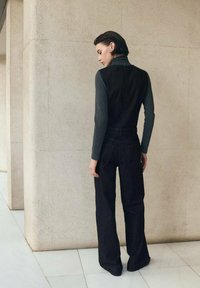 Jeans negros de pierna ancha combinados con un top ajustado de manga larga en gris oscuro. El conjunto presenta un diseño elegante y minimalista que contrasta en color y textura.