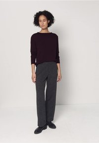 Pull en tricot couleur bordeaux à coupe décontractée, associé à un pantalon large gris foncé en tissu texturé. Des chaussures noires complètent la tenue.