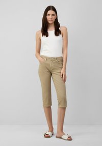 Pantaloni a vita alta beige in cotone, con chiusura anteriore a bottone e cerniera, dotati di tasche laterali, abbinati a una canotta bianca a costine.